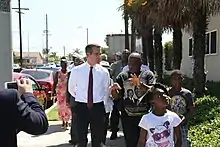 Un homme blanc en chemise et cravate, Eric Garcetti, marche sur un trottoir aux côtés d'un groupe de personnes noires de tous âges dont un homme qui lui parle.