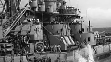 Photographie du côté de la superstructure d'un navire où se trouvent cinq tourelles doubles. Deux d'entre elles ont leurs canons pointés vers le ciel.