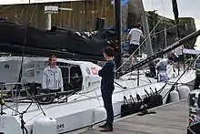 Debout à l'arrière du bateau, Dutreux converse avec un homme qui se trouve sur le ponton.