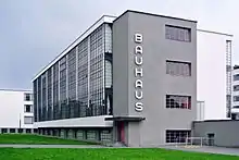 Photographie en couleur d’un bâtiment vu de trois-quart. Béton et façade en baies vitrées.