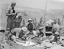 Sept hommes en treillis militaire utilisant des radios et des mégaphones.