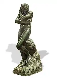 L'image représente une sculpture d'Eve en bronze dans une position pudique et honteuse. Sa tête et ses épaules sont baissées. Elle couvre de son bras droit sa poitrine et se protège le visage de sa main gauche.