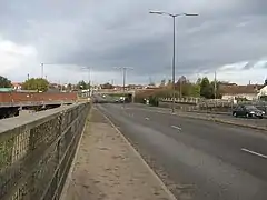 Photo prise depuis le trottoir d'une route à quatre voies avec quelques voitures en circulation, sous un ciel gris