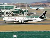 À l'atterrissage, un Boeing 767-300 Asiana Airlines avec la livrée Star Alliance. Un Boeing 777 Korean Air se trouve à l'arrière-plan.