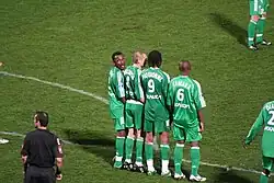 4 joueurs en vert formant un mur, l'arbitre étant positionné derrière celui-ci.