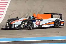 Photographie d'une voiture de sport-prototype bleu, noir et orange, vue de trois-quarts, sur une piste.