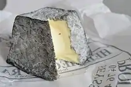Photographie en couleurs d'un fromage cendré en forme de pyramide tronquée.