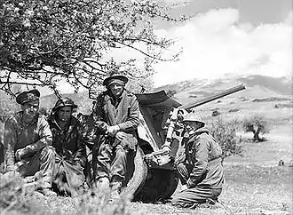 Quatre soldats, accroupis ou debout, posant devant un canon dans leur dos.