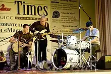 trois musiciens sur scène : un percussionniste, un bassiste électrique, un batteur