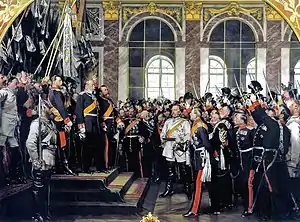 Tableau d'Anton von Werner: proclamation de l'empire allemand par l'empereur Guillaume Ier le 18 janvier 1871 avec Bismarck (en uniforme blanc) dans la galerie des glaces du château de Versailles. Bismarck est au pieds des marches menant à l'empereur, les deux hommes sont entourés d'une foule nombreuse.