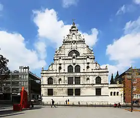 Façade baroque triangulaire d'une église donnant sur une vaste place urbaine.