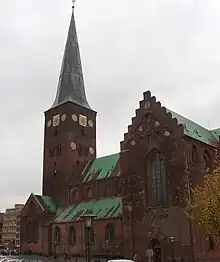Photo représentant une cathédrale en brique rouge aux toits verdâtres.