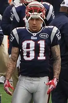 Aaron Hernandez en tenue de football américain, maillot 81, et un casque sur la tête.