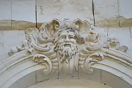 Sculpture de pierre blanche représentant un visage d'homme barbu entouré de feuilles.