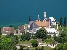 Photographie couleur d'un ensemble de bâtiments comportant une église, observés depuis un point haut, avec un lac en arrière-plan.