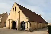 Photographie en couleurs d'une large grange en calcaire avec un toit à deux pans, et deux portes voûtées.