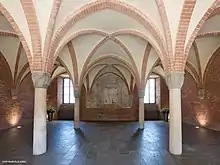 Photographie couleur d'une salle voutée en ogives de briques.