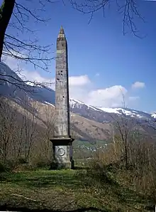 Photographie en couleurs d'un obélisque devant des montagnes enneigées.