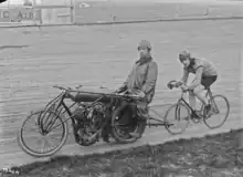 Cycliste en piste sur un vélodrome, derrière une moto.