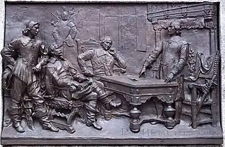 Photographie d'un bas-relief en bronze présentant plusieurs personnages autour d'une table, deux hommes se tenant debout, les deux autres assis.