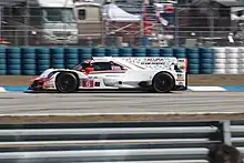 Voiture de course blanche, de profile, se dirigeant vers la gauche, avec un mur de pneus en fond.