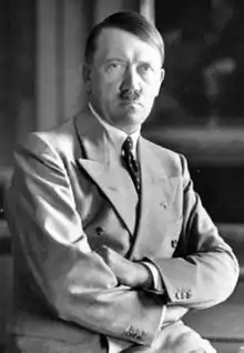 Photo portrait noir et blanc d'Adolf Hitler en costume deux pièces clair, assis de face, les bras croisés sur son ventre.