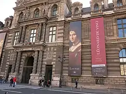 Photographie d'une façade d'un bâtiment classique portant de grands panneaux annonçant une exposition.