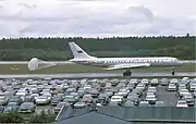 photographie en couleur d’un avion sur une piste d’atterissage bordée d’un parking, un parachute étant déployé à l’arrière