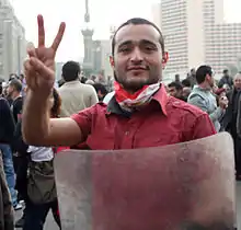 Ahmed Douma de face, faisant d'une main le V de la victoire et tenant de l'autre un bouclier