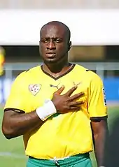 Un joueur de football en tenue, maillot jaune et short vert, main sur le cœur.