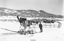 Photo en noir et blanc d'un avion sans ailes sur la neige, un homme s'appuyant sur sa queue.