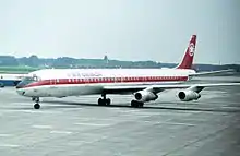 Douglas DC-8, livrée blanche et rouge. L'avion est très similaire au 707, l'absence de l'antenne « pique » au sommet de la dérive est la différence visuelle la plus évidente.