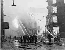 Des pompiers dirigent leurs lances vers des bâtiments en feu à Manchester après une attaque aérienne.