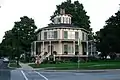 Grande maison à ossature bois, toit en pente et lanterne, véranda tout autour. Les fenêtres cintrées et les volets de fenêtre ajoutent à l'effet décoratif.  La Rich-Twinn Octagon House, Akron, New York.