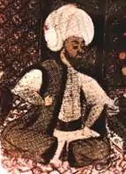Miniature en couleurs représentant un homme en turban assis sur un tapis.