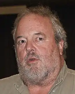Photo d'un visage d'une cinquantaine d'années avec une barbe de trois jours et les cheveux grisonnant, regardant au loin.