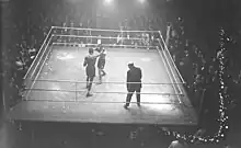 Photographie en noir et blanc prise de haut d'un combat de boxe.