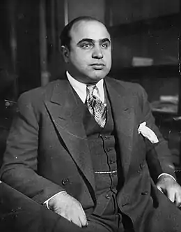 Photographie en noir et blanc d'un homme assis vêtu d'un costume.