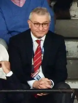 Un homme assis, vêtu d'un costume et d'une cravate.