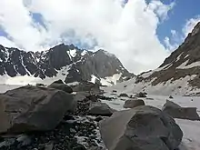 Blocs rocheux et cailloux reposant sur un glacier avec des montagnes en arrière-plan.