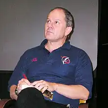 Homme aux cheveux gris avec un polo bleu.