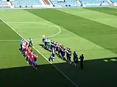 vue d'un terrain de football avec une haie d'honneur de joueurs aux maillots bleus et blancs