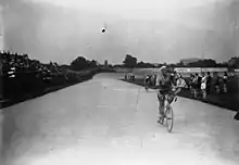 Photographie en noir et blanc d'un coureur cycliste effectuant un tour d'honneur à vélo, un bouquet à la main.