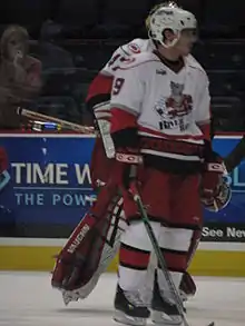 Photograpgie d'un joueur de hockey sur glace avec un maillot blanc frappé d'un rat tenant une crosse.