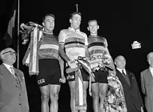 Photographie en noir et blanc montrant trois cyclistes sur un podium entourés par deux officiels.