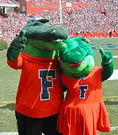 Mascottes à taille humaine, représentant deux alligators verts avec un tee-shirt rouge marqué d'un F, on peut voir un stade en arrière-plan.