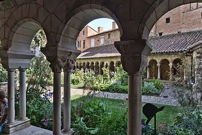 photo couleur d'arcs romans portés par des colonnettes jumelées. À travers les ouvertures, on distingue le jardin du cloître de type médiéval et d'autres arcades.
