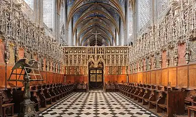 Photo couleur des sièges en bois en deux rangées face à face enserrées dans un écrin de pierre ciselée, au cœur d'une église dont les voutes sont peintes majoritairement de bleu.