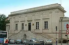 Photo couleur d'un bâtiment d'architecture classique à un seul étage et entrée surélevée desservie par un perron. Une corniche au sommet des murs masque la toiture.