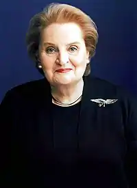 Pale-skinned woman wearing a dark blouse and coat, with an eagle badge on her left shoulder